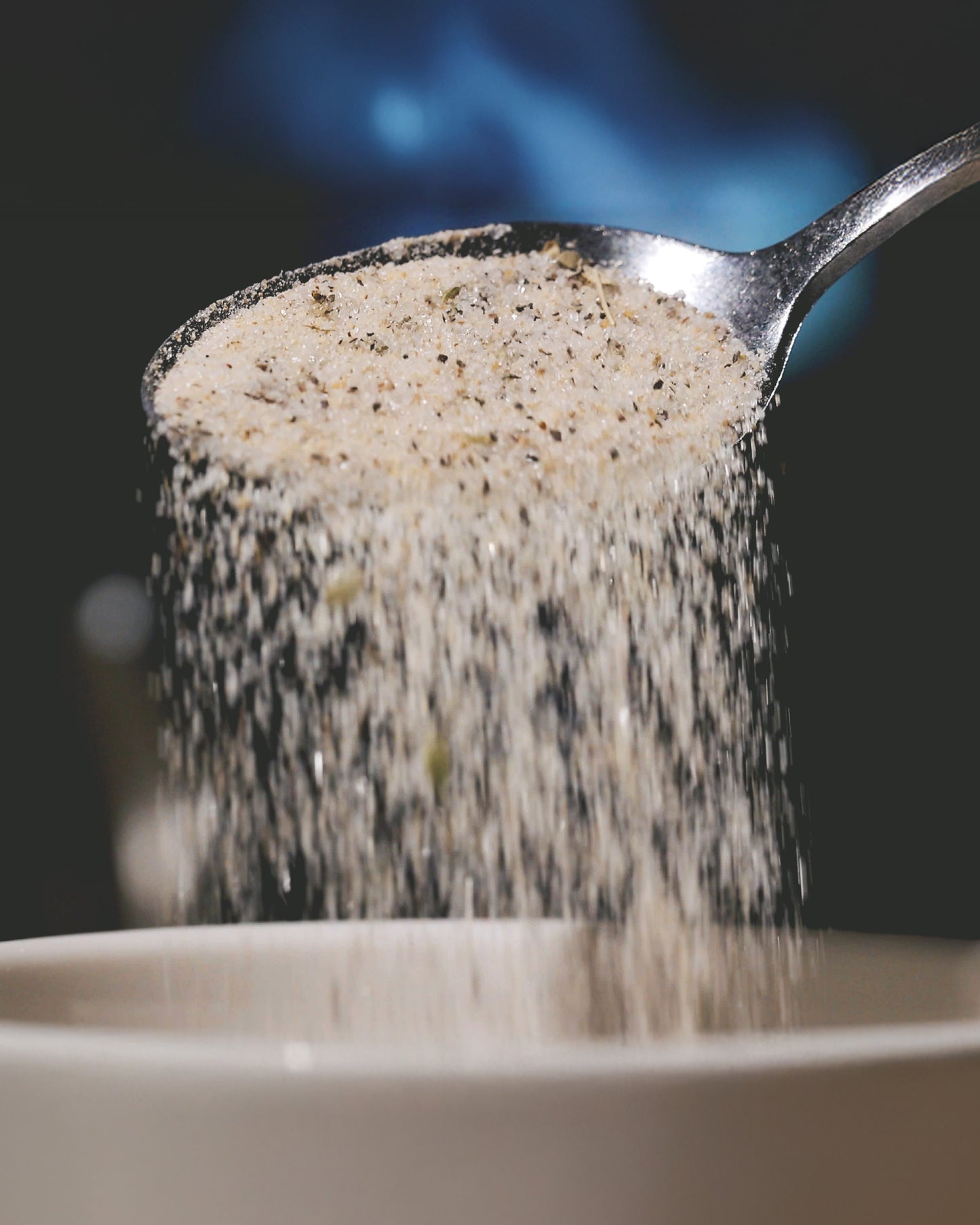 A spoon shaking Crazy Tony's seasoning into a white bowl.